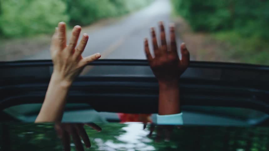 Point of view pair of hands waving out of sunroof while driving on tree lined road