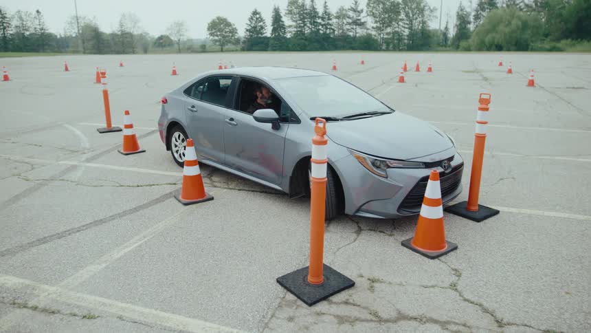 Instructor with a woman inside the car that is reversing and hitting a cone