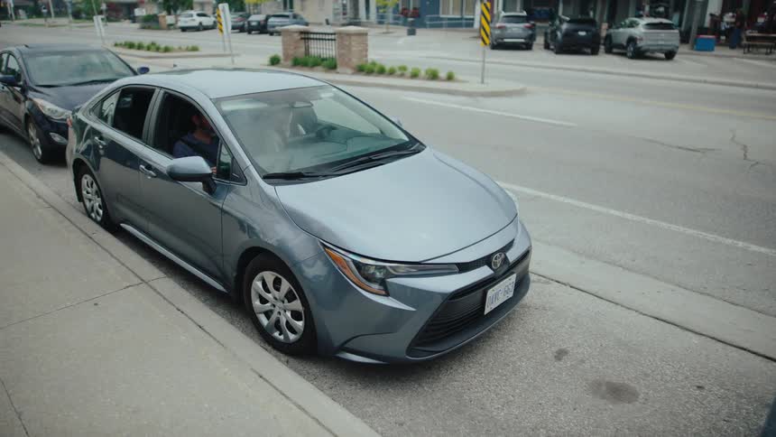 Gray sedan car with two people inside being parked in a street parking space