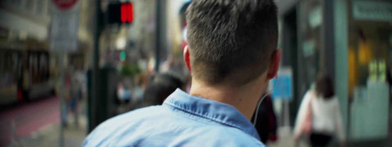 A man wearing earphones walks down a crowded city sidewalk
