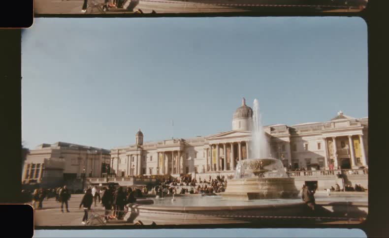 People relax on wide stone steps surrounding the trafalgar square fountain with the national gallery visible in the background
