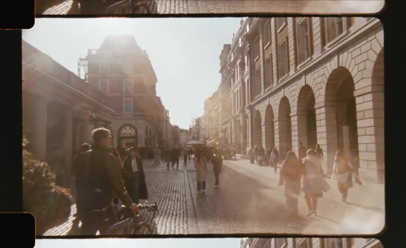 A busy street possibly in europe is filled with pedestrians and historic buildings under a bright sky the warm sunlight casts long shadows giving the scene a vibrant perhaps lateafternoon or earlymorning atmosphere