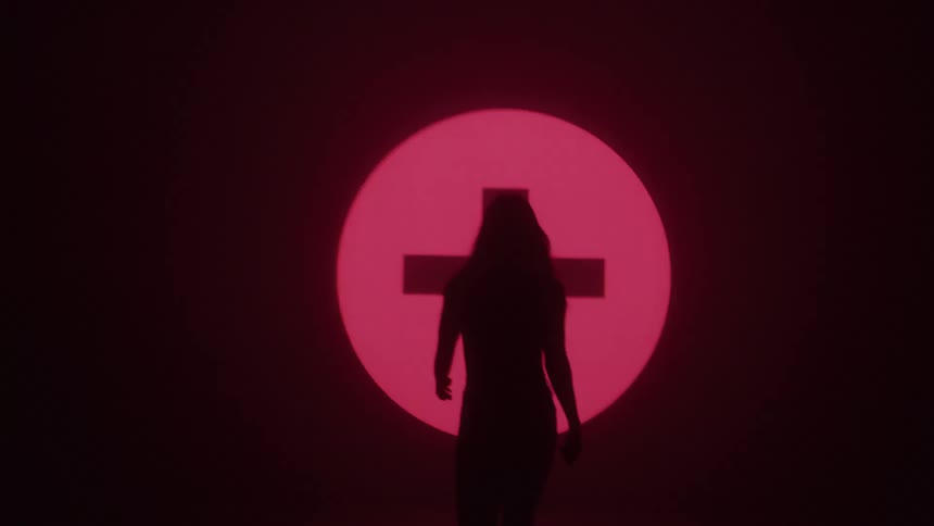 Silhouette of a woman walking towards a wall displaying objects on a screen