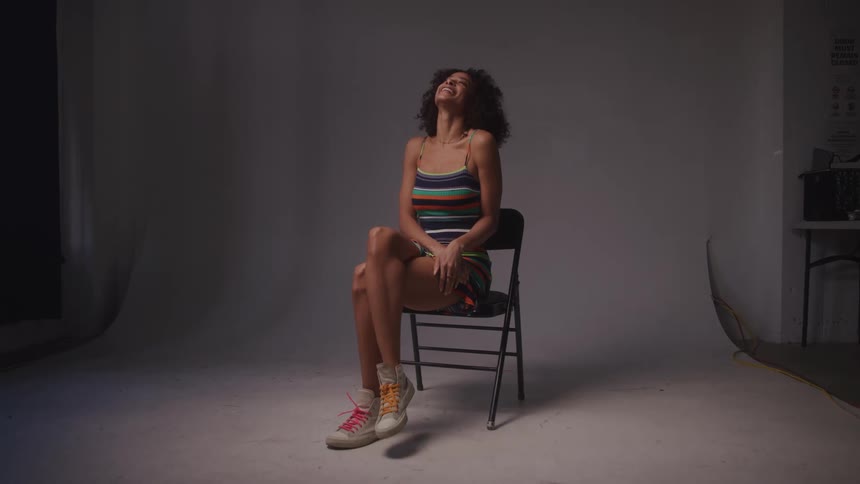 A young woman sits in a folding chair while posing and smiling
