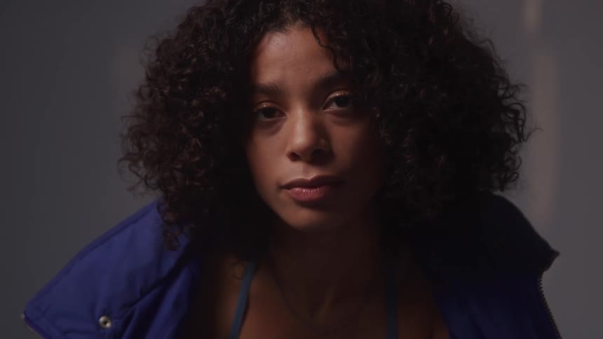 A woman with curly black hair tilts her head to the side while looking forward