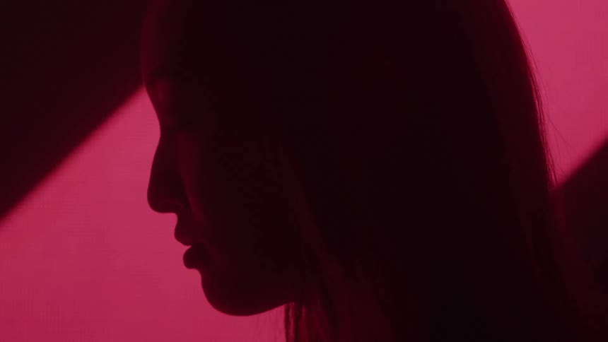 A womans silhouette is illuminated in profile by a pulsing red light