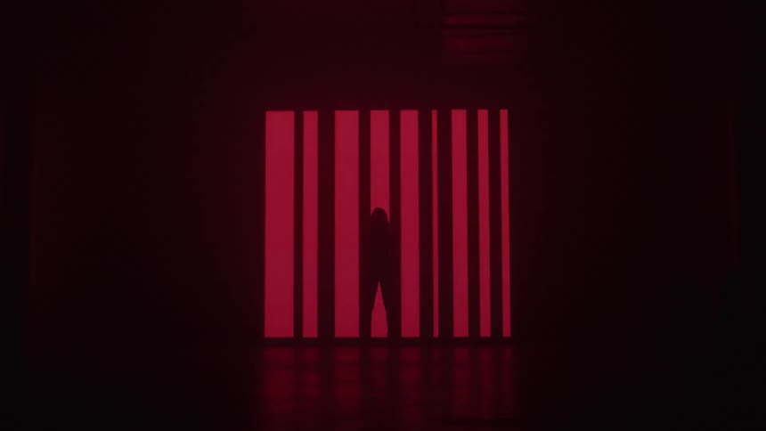 A silhouetted person stands before a large screen displaying red symbols on a dark background