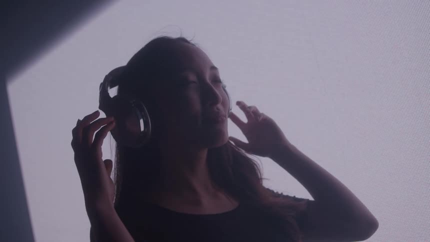 Woman with eyes closed enjoying the experience with headphones in a dark room environment with a screen in the background