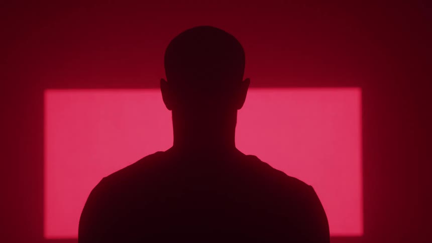 From behind a man is silhouetted against a red wall where large animated arrow graphics are projected and move across the screen