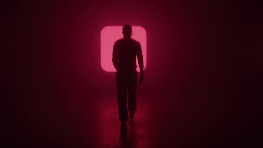 The man is walking towards the flashing symbols on the wall
