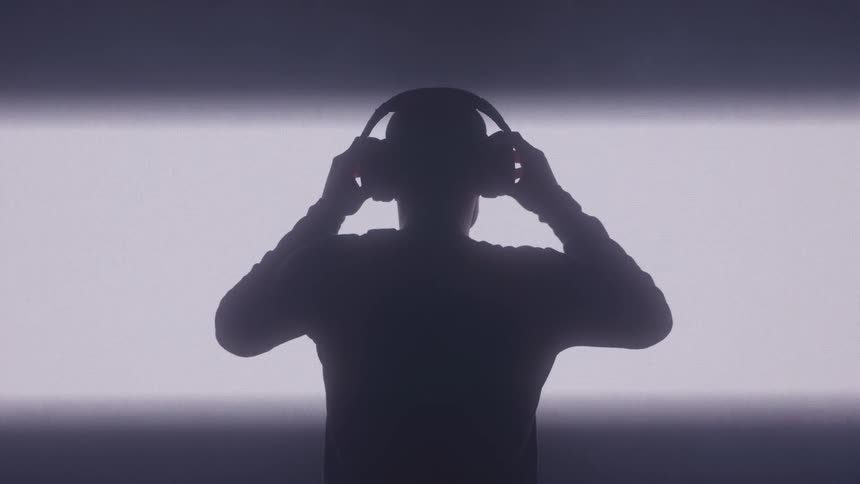 Silhouette of a man facing a white screen putting on headphones