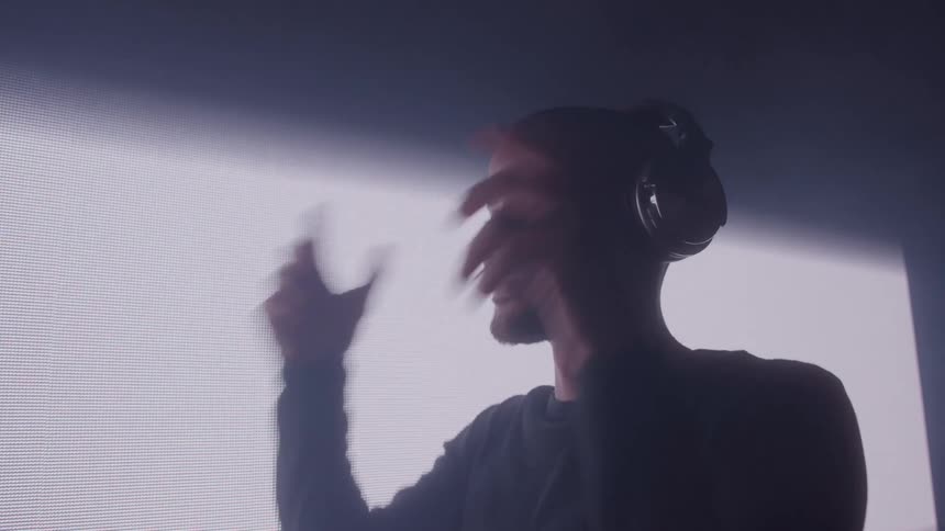A man wearing headphones performs in front of a bright led screen
