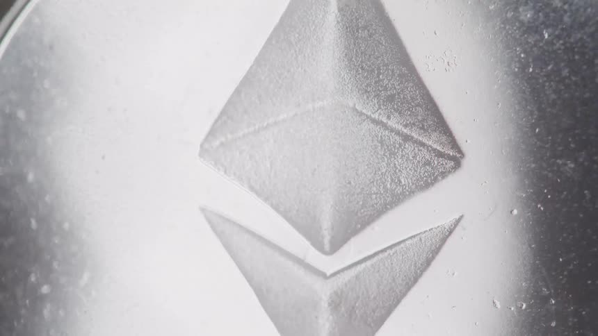 A shiny metal coin displays an angular logo imprinted on its face