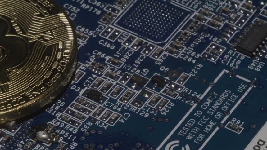 A closeup tracking shot moves across a blue computer circuit board where a physical gold bitcoin rests symbolizing digital currencys link to technology