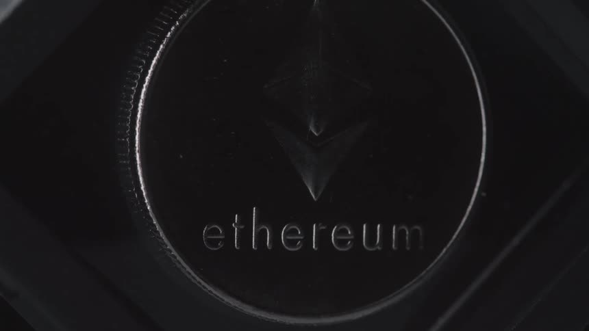 A closeup of a dark metallic ethereum coin shows its logo and engraved name