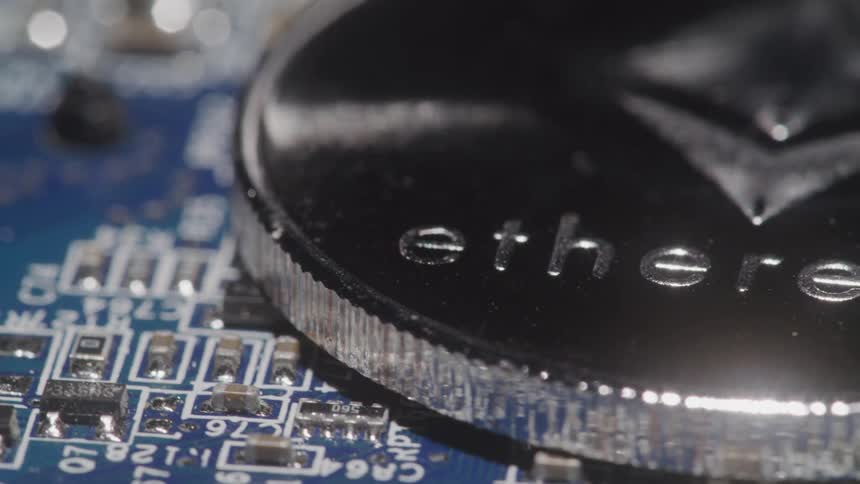 A metal coin imprinted with etherium on its face it atop a circuit board