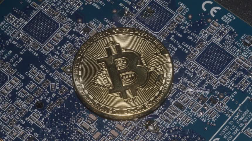 A gold bitcoin token placed on a blue computer motherboard