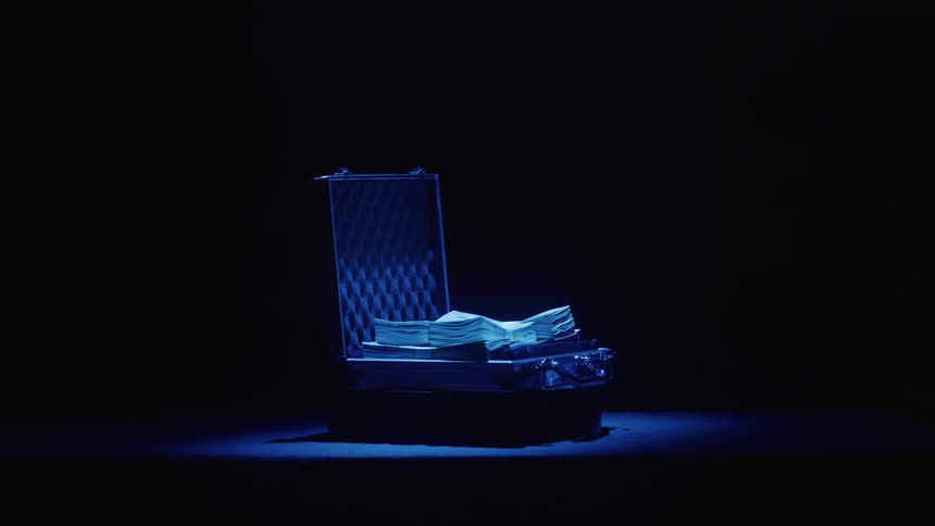 A suitcase filled with stacks of cash glows under dramatic blue lighting in darkness