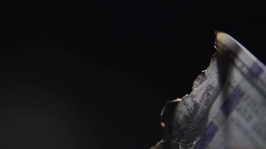 A burnt 100 bill lies curled and smoldering its ink partially singed