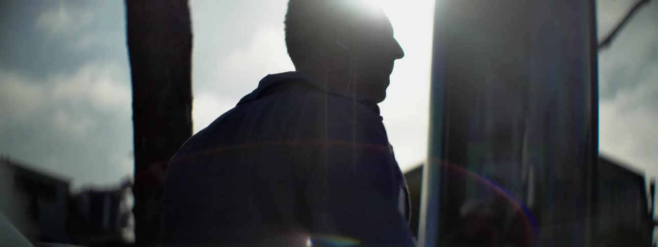 A man wearing ear buds walks outside under trees