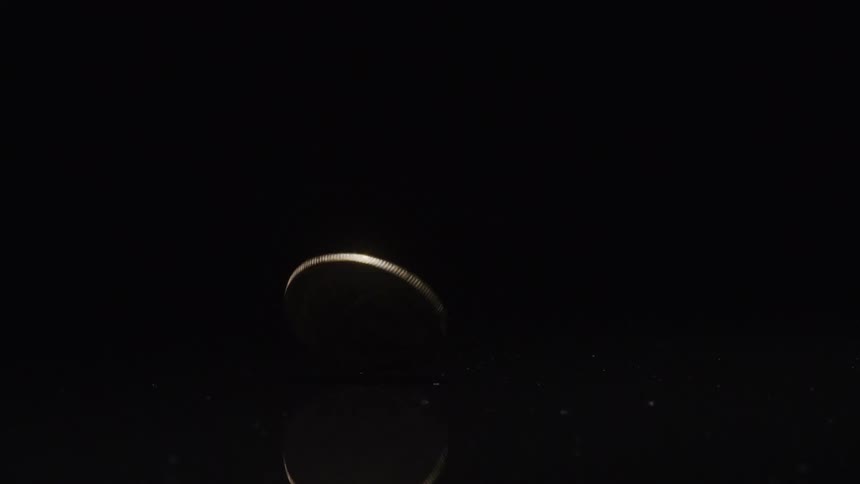 A shiny coin with the bitcoin logo on it spins on its edge atop a reflective surface