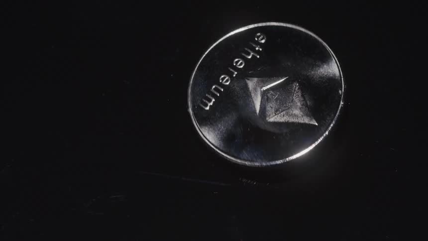 A polished silver ethereum cryptocurrency coin is shown spinning and reflecting light on a dark reflective surface the closeup shot highlights the distinct ethereum logo and text emphasizing its digital and tangible presence