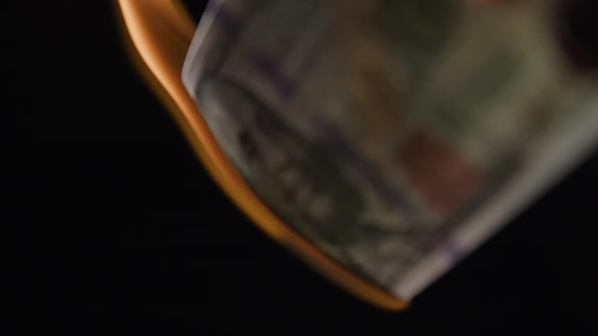 A one hundred dollar bill is slowly consumed by a burning flame