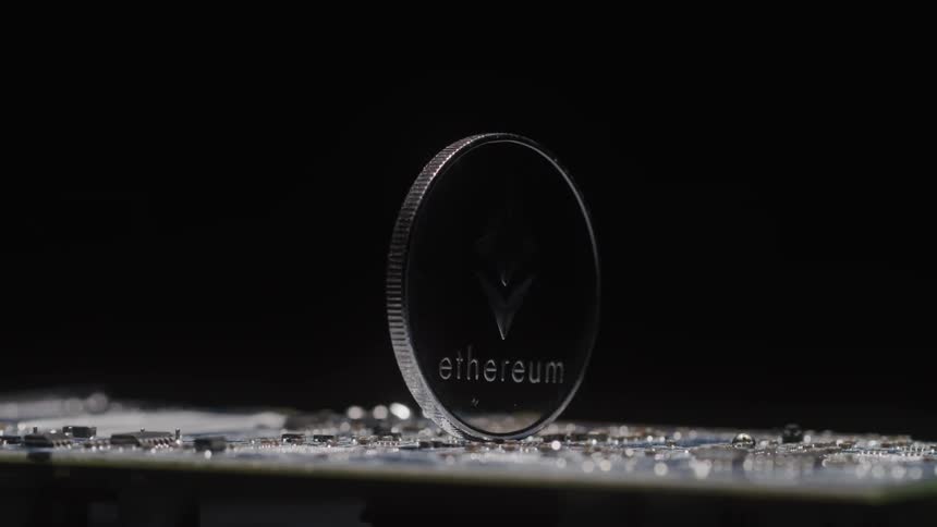 A closeup shot shows a physical ethereum coin rotating while balanced on a printed circuit board