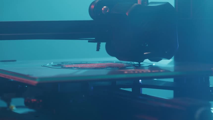A 3d printer printing something on a flat surface and everything is lit up blueish