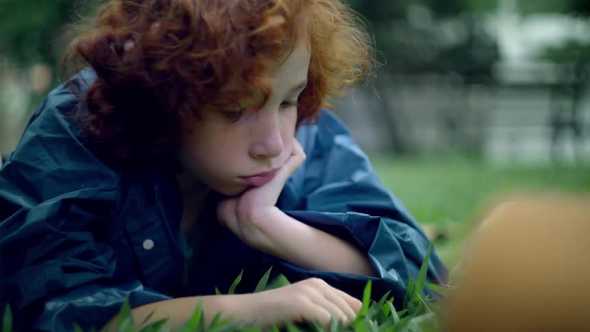 Close up of a male teenager playing with the grass while lying on a field outdoors during daytime