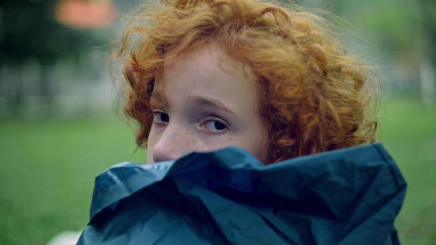 A girl with curly red hair peers over a blue blanket with wide eyes