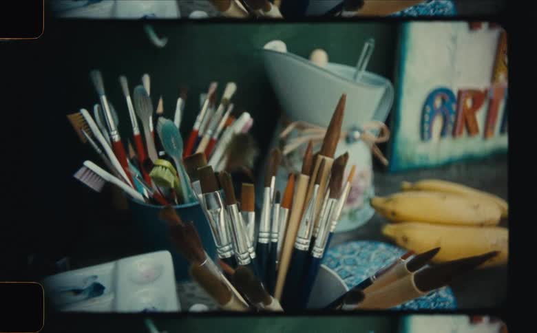 Toothbrushes and paintbrushes fill a container sitting on a table near a bunch of bananas in an art studio
