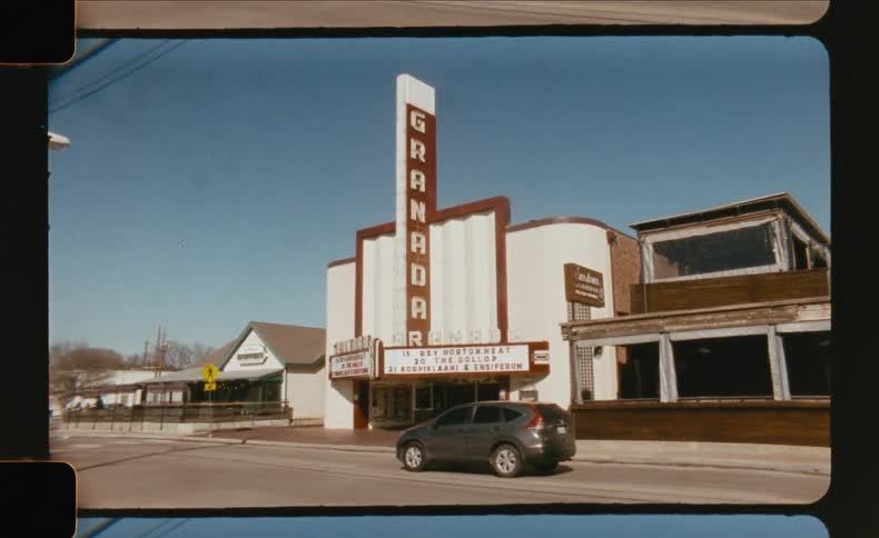 A wide shot captures the art deco facade of the granada movie theater on a sunny day with the entire frame bordered by the edges of a film strip
