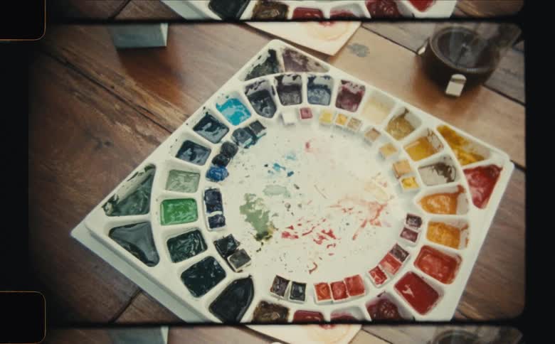 A palette with various watercolor paints arranged in a circular pattern on a wooden table
