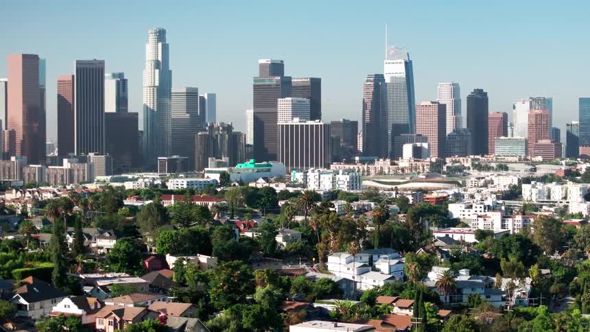 The iconic downtown los angeles skyline rises behind a lush green residential neighborhood on a clear sunny day