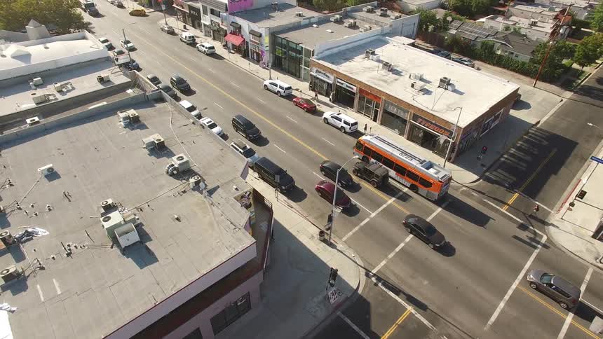 An aerial view captures midday traffic and palm trees along a busy urban Melrose Avenue in Los Angeles