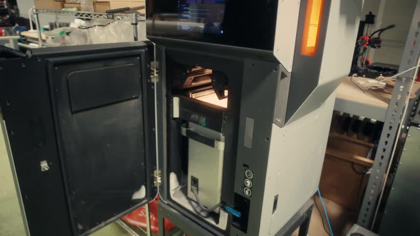 A person wearing gloves opens the door of a machine in an industrial warehouse setting