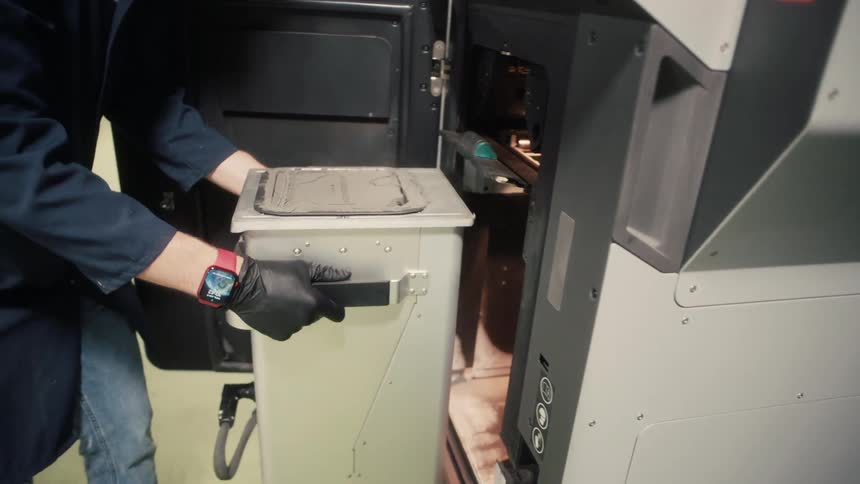 Worker removes a container from a machine and carries it toward a plastic enclosed area