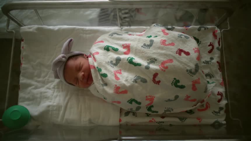 A baby wrapped tightly in a blanket squirms around in a hospital crib