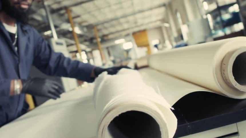 A closeup shot of large rolls of a reddishbrown material possibly paper or fabric being fed into industrial machinery hands are briefly visible guiding the material suggesting a manufacturing or production process