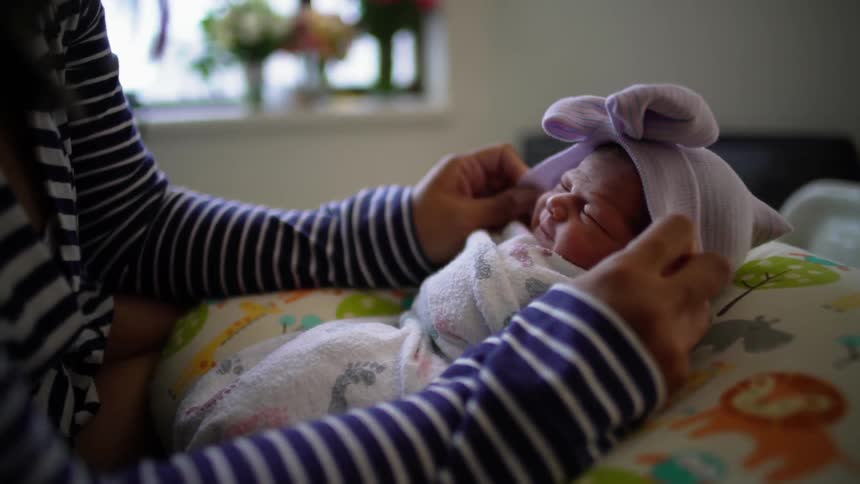 A mother adjusts the hat of a swaddled newborn