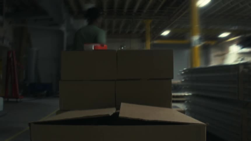 Male worker moves boxes around a factory with a platform truck