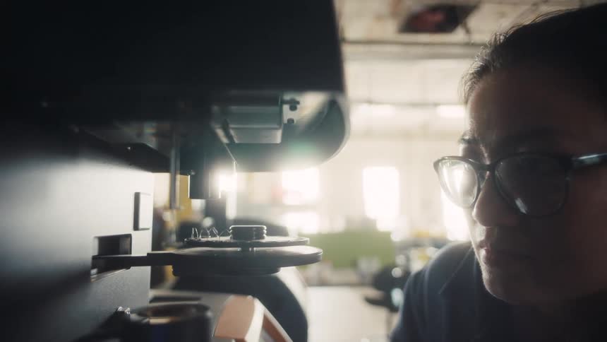 A worker inspects a rotating circular component inside a machine within a workshop