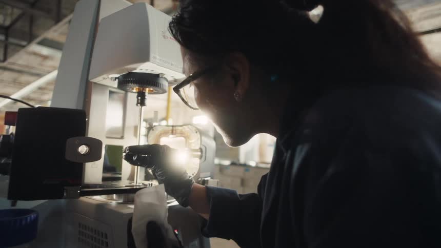 Female technician closely inspecting a component under a precision testing machine