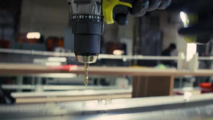 Close up of a person drilling a hole into a metal with a hand drill in a factory