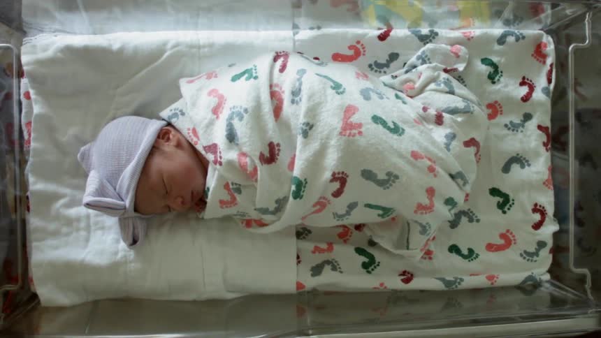 A newborn baby sleeps in an incubator