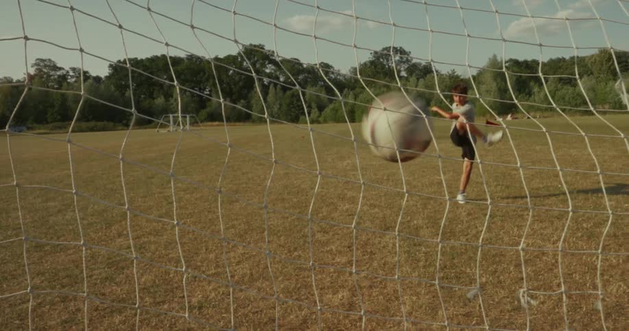 Two kids are kicking soccer balls into an outdoor net