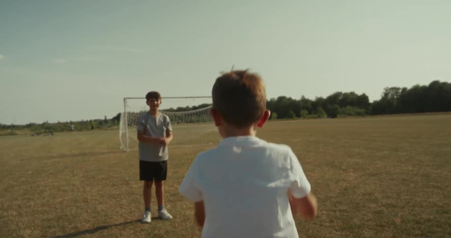 Two boys play soccer in a field with one throwing the ball to the other who controls it with his chest