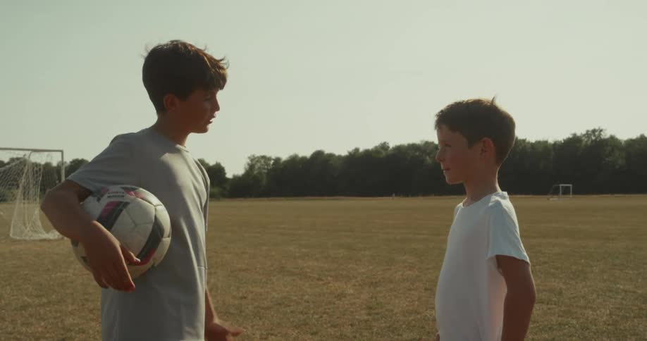 Two kids are talking while standing on a soccer field