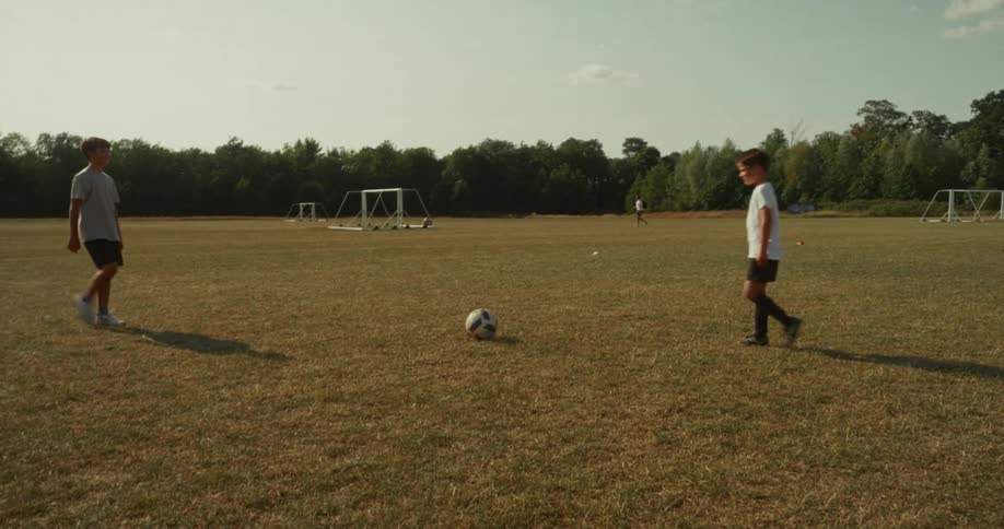 Two children shake hands over a soccer ball at midfield with the goalpost visible in the background